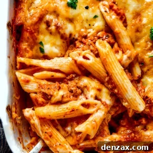Scooping out a spoonful of baked mostaccioli from a large baking dish.