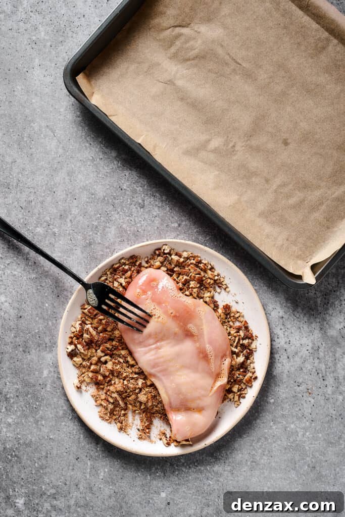 Raw chicken being coated in a ground pecan mixture.