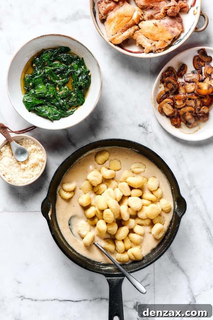 Gnocchi and cream sauce in a skillet, next to dishes of spinach, mushrooms, and chicken.