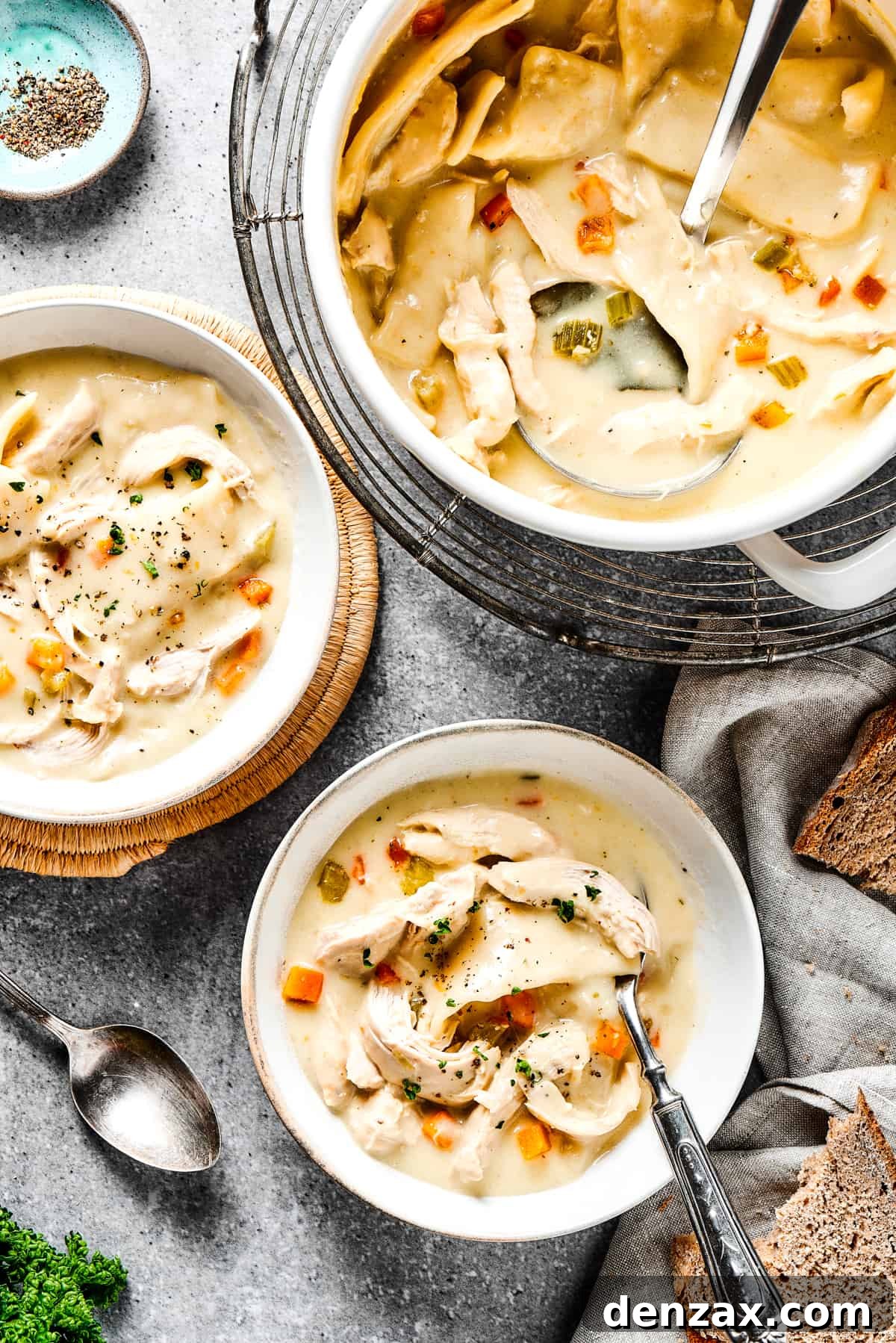 Creamy chicken and dumplings in a pot, along with two bowls of the dish.