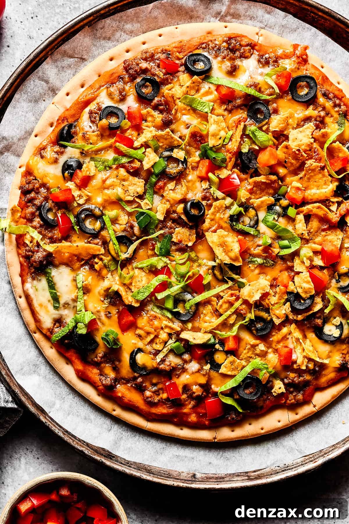 A baked taco pizza with toppings sprinkled over it.