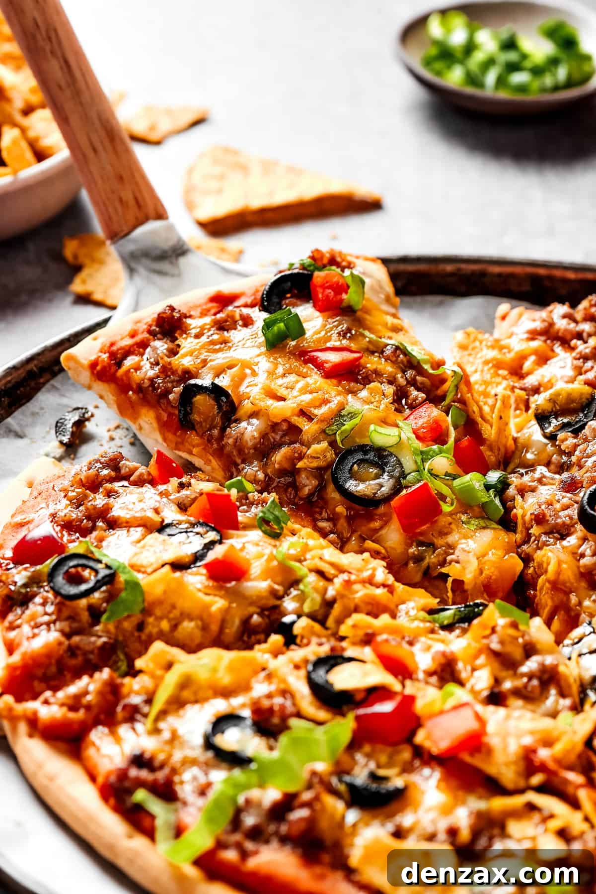 Lifting a slice of taco pizza with a pie server.