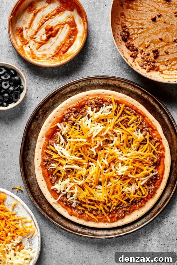 A pizza crust topped with refried bean sauce, beef, and cheese.