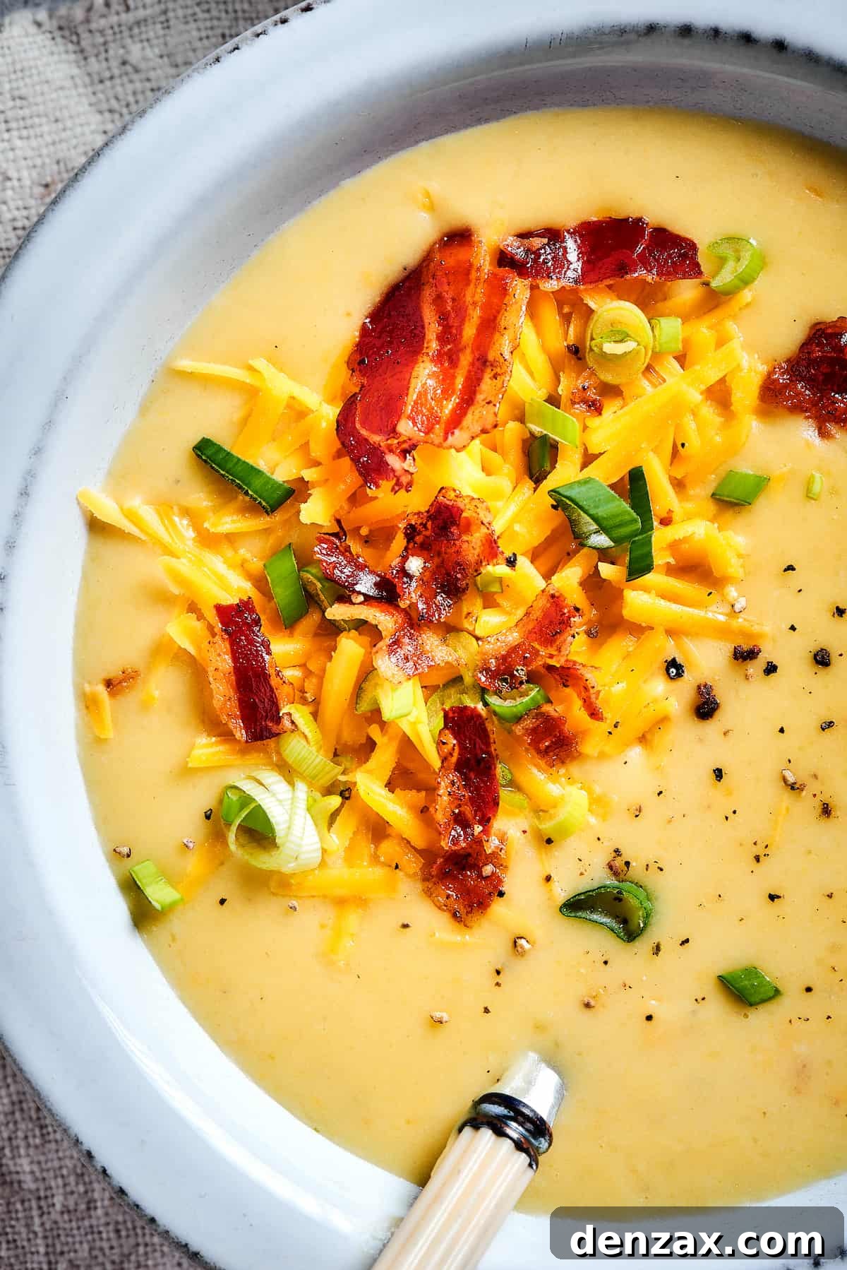 Close-up shot of bacon, green onions, and cheese sprinkled into a bowl of creamy soup.