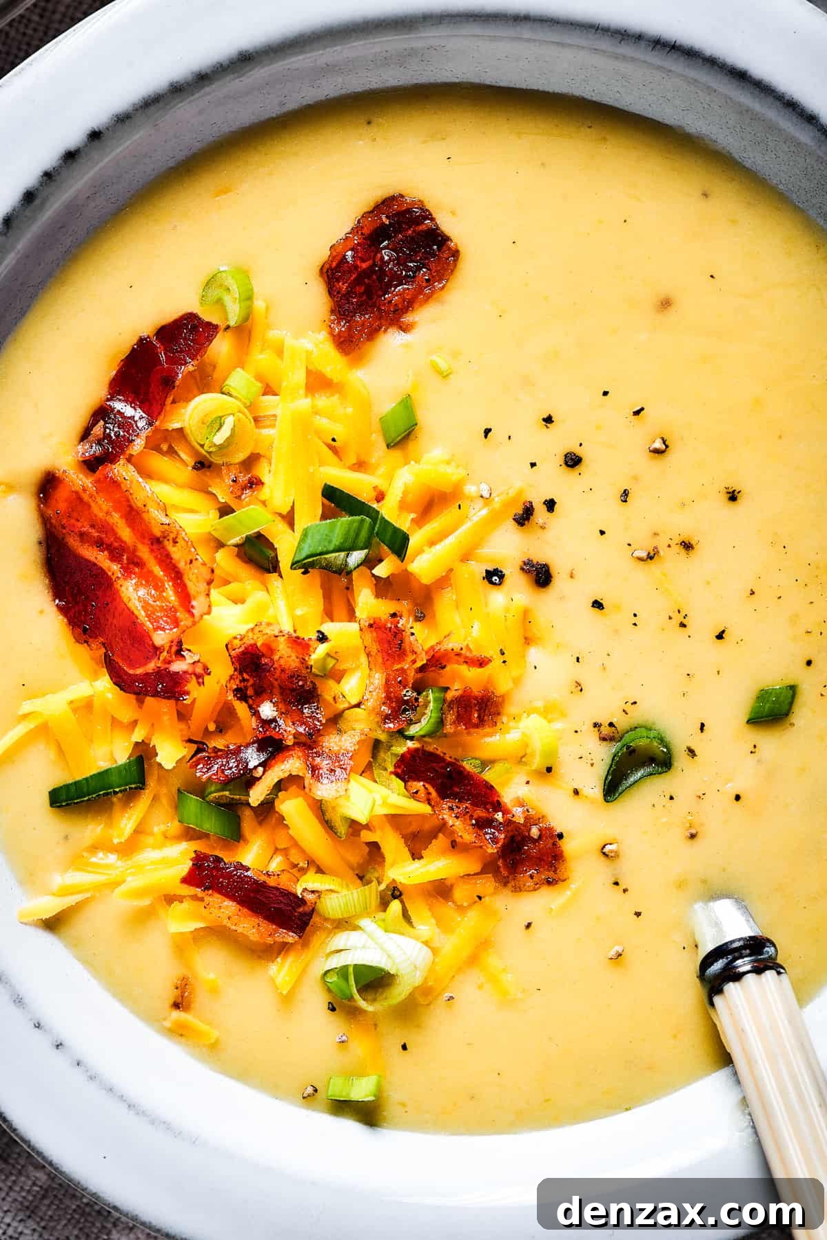 Close-up shot of bacon, green onions, and cheese sprinkled into a bowl of creamy soup.
