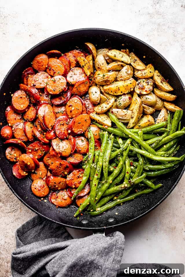 grey linen kitchen towel next to a black skillet filled with andouille sausage slices, potatoes, and green beans