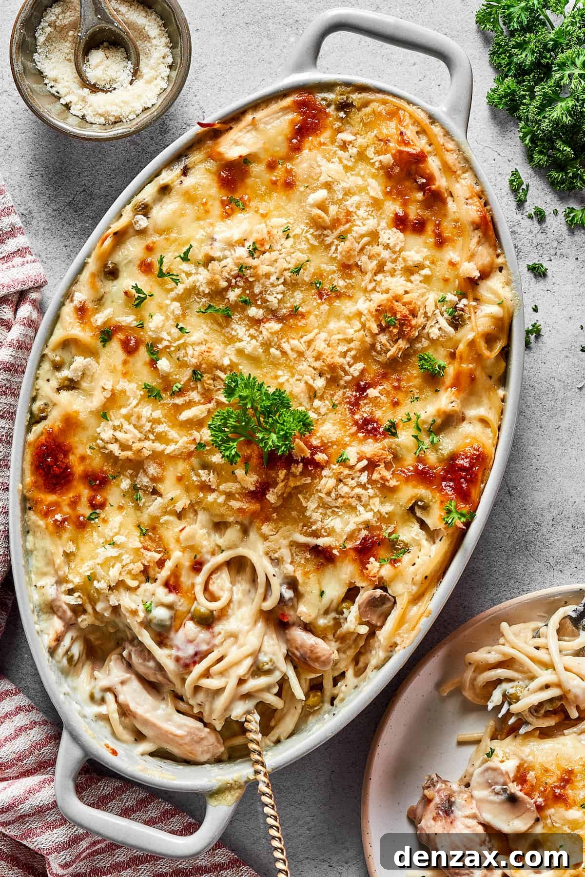 A large chicken tetrazzini casserole next to a dinner plate and a bunch of fresh herbs.