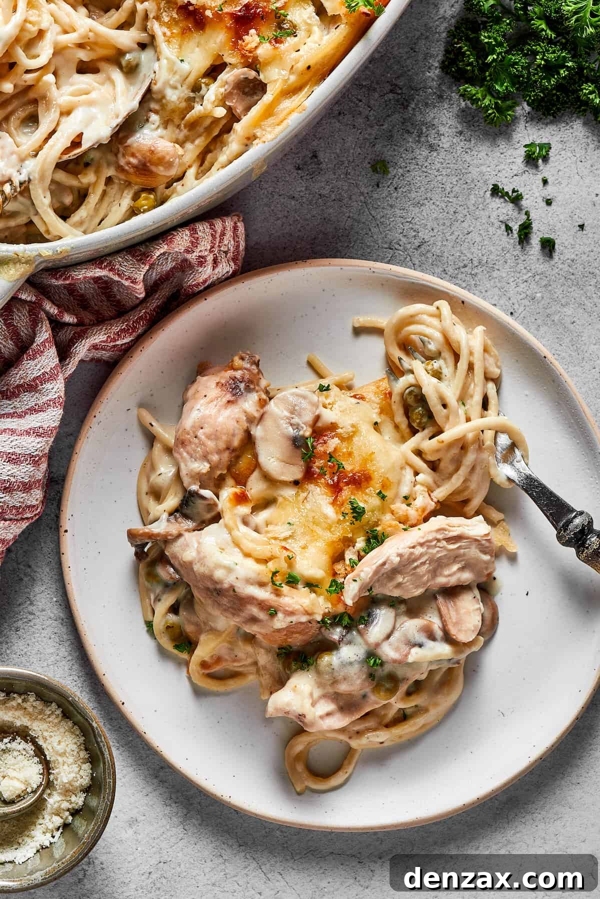 A dinner plate of pasta casserole next to the larger casserole dish, on a white table.