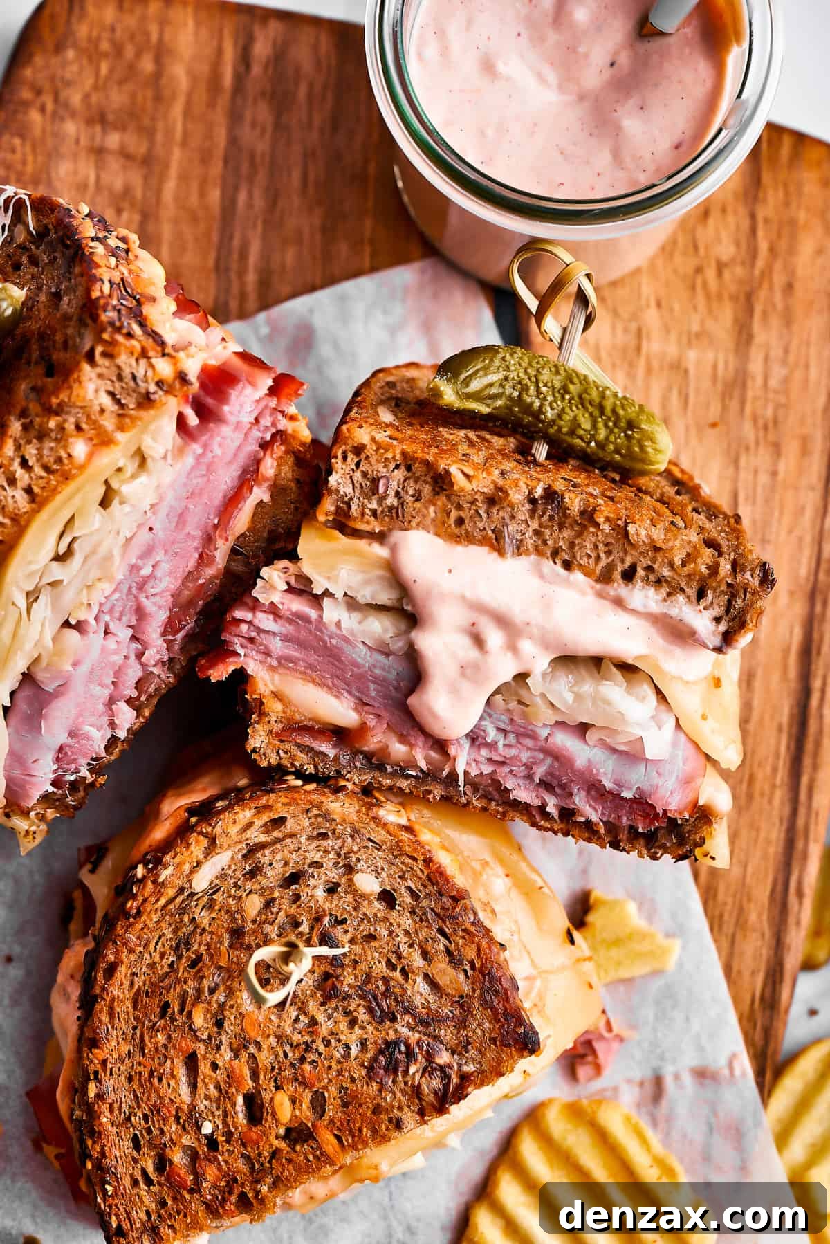 Three Reuben sandwich halves, some potato chips, and a jar of dressing on a cutting board.