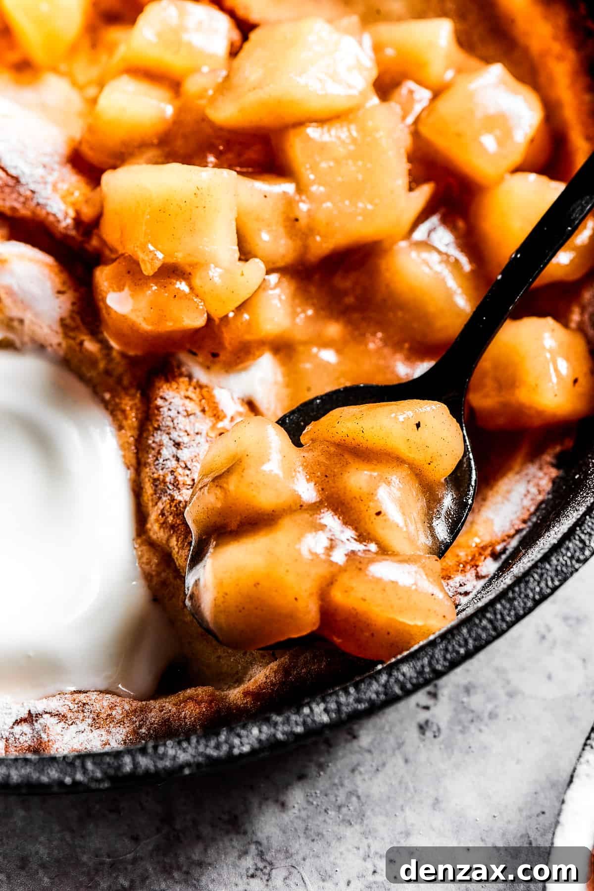 spooning apple pie filling on top of a dutch baby pancake.