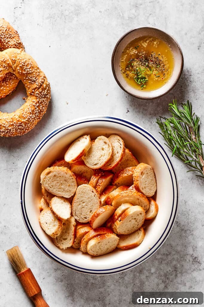 Sliced bagel rounds next to a dish of seasoned butter and a sprig of rosemary.