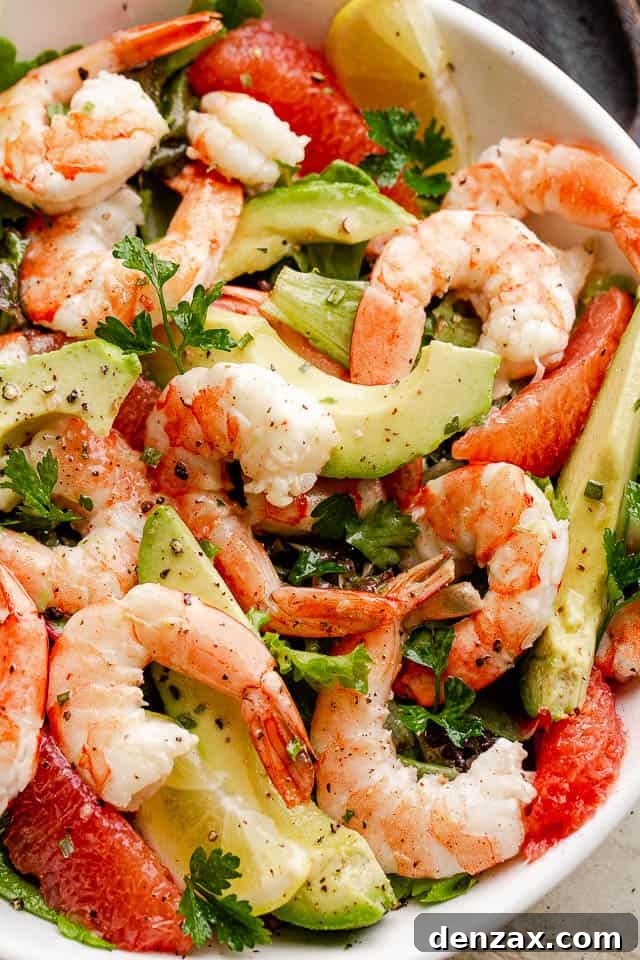 cooked shrimp, avocado slices, and salad greens tossed together in a white serving bowl