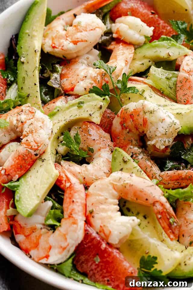 cooked shrimp, avocado slices, and salad greens tossed together in a white serving bowl