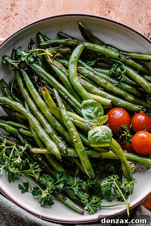 This sauteed green beans recipe is a delicious, quick, and easy veggie side dish! The butter and garlic add a rich and savory flavor. cooked green beans served in a bowl with fresh basil and cherry tomatoes