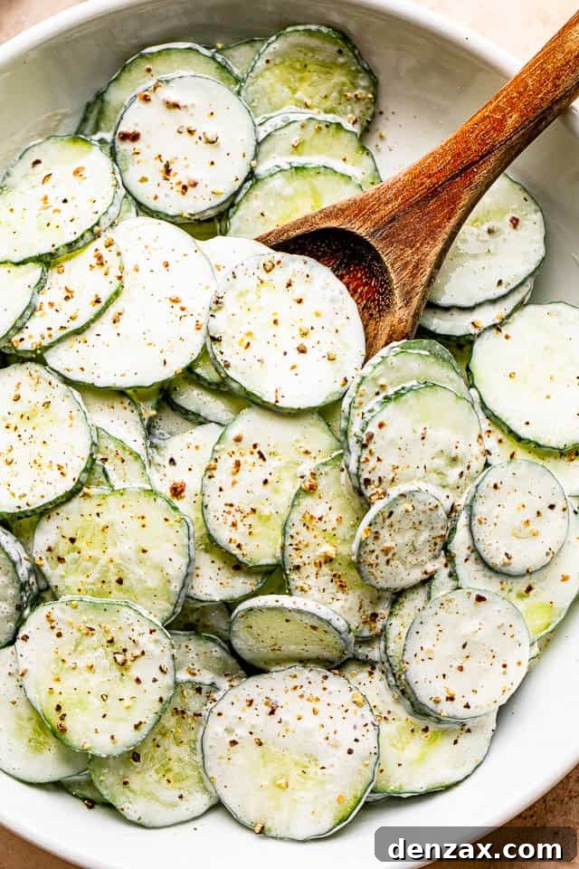 salad bowl filled with sour cream covered cucumbers sprinkled with cracked black pepper on top.