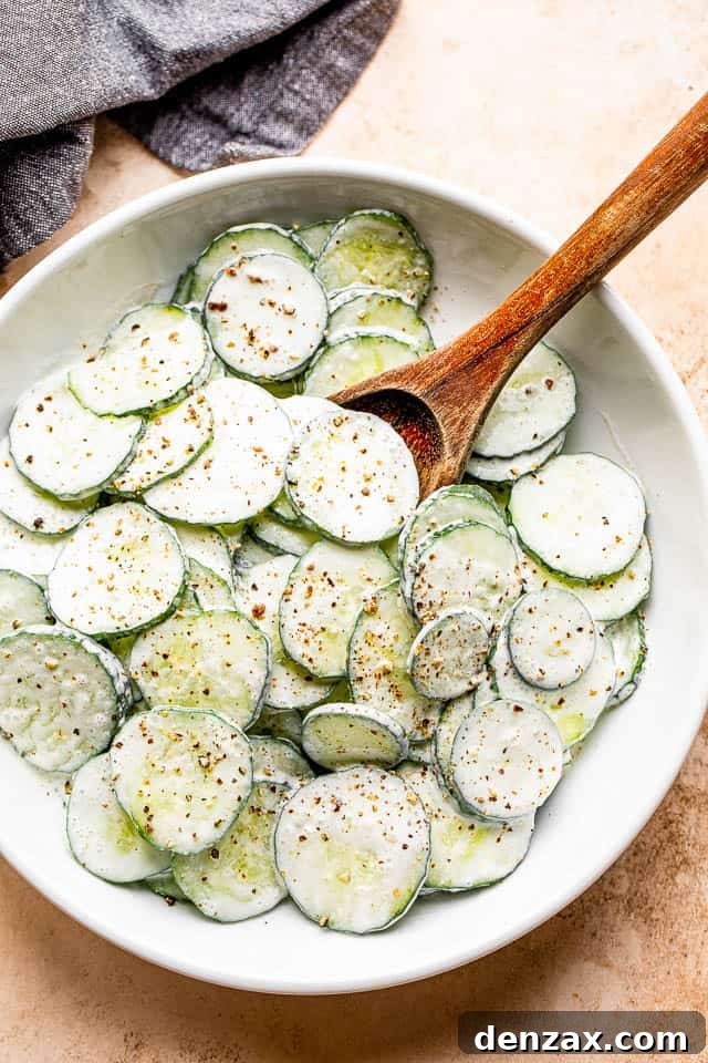 wooden spoon mixing cucumbers in a white salad bowl tossed with sour cream