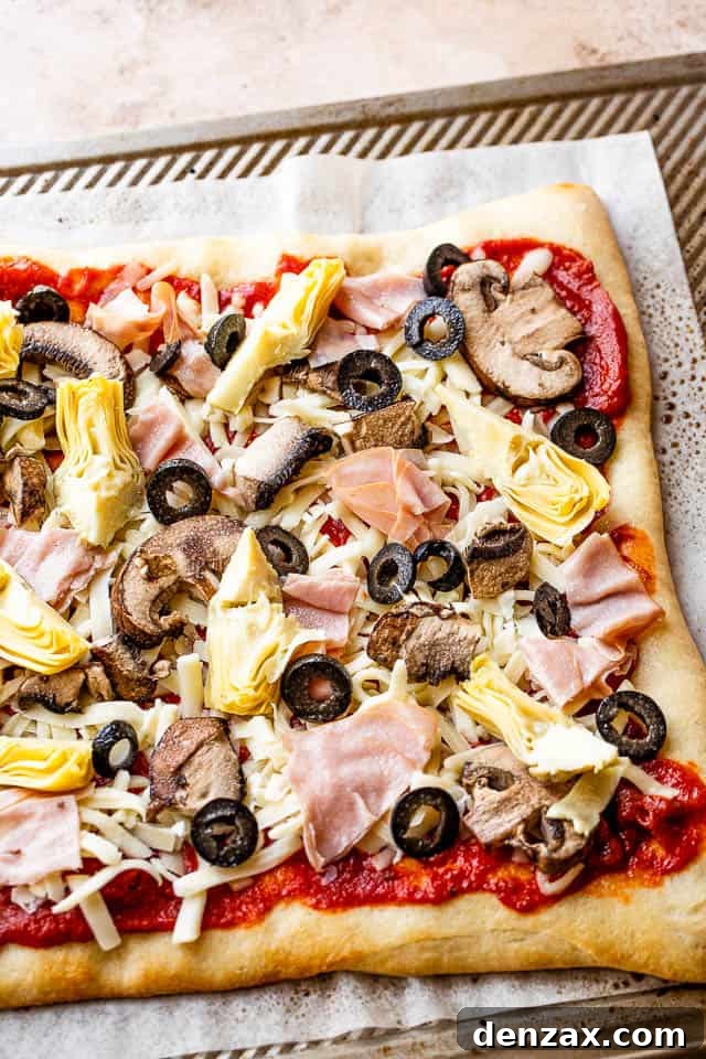 tomato sauce, cheese, artichoke hearts, olives, and ham on top of pizza crust prepared for grilling