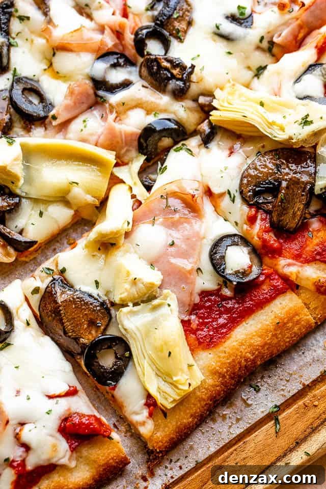 top view of square slice pizza topped with ham, olive slices, and artichoke hearts
