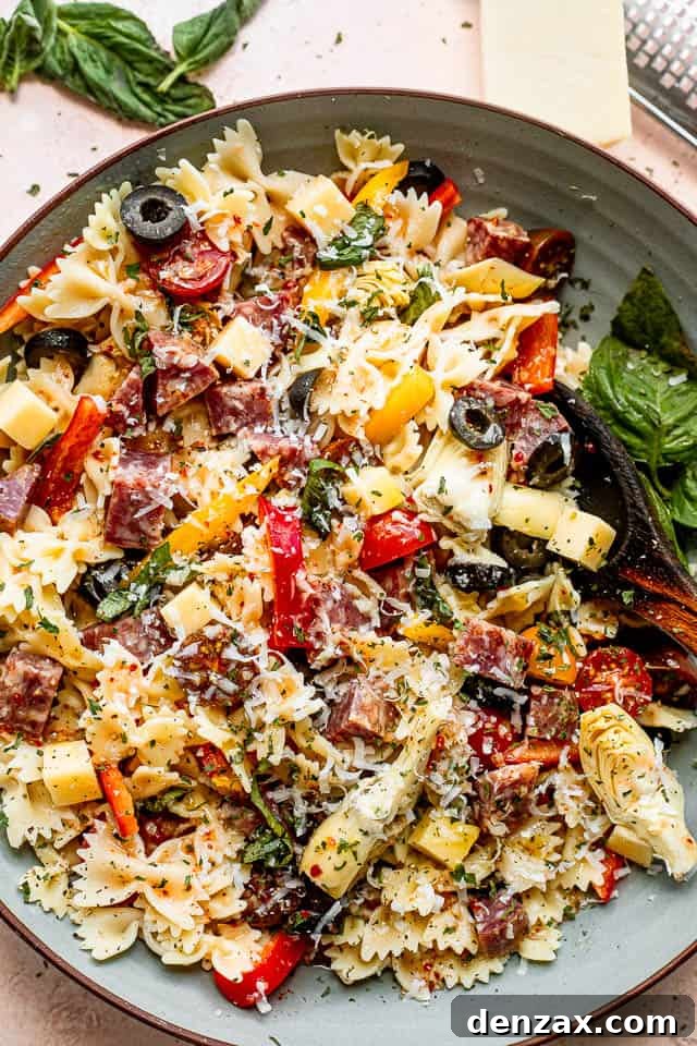 top view shot of a wooden spoon in a bowl filled with pasta, cheese cubes, salami cubes, tomatoes, and olives
