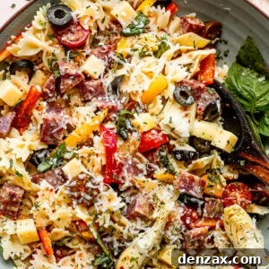 top view shot of a wooden spoon in a bowl filled with pasta, cheese cubes, salami cubes, tomatoes, and olives