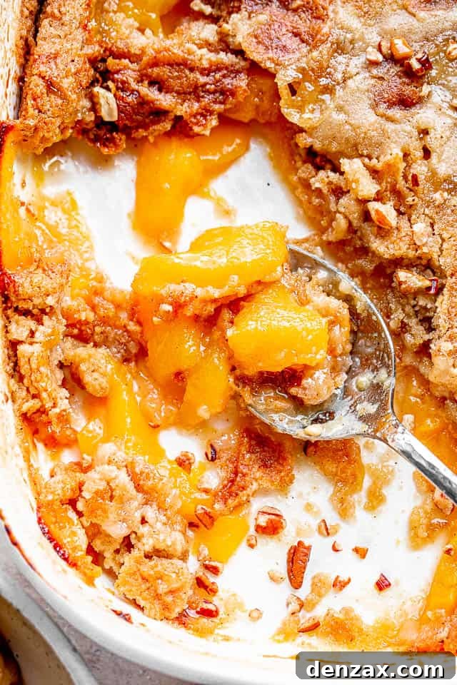 Homemade Peach Dump Cake Recipe — Simple From-Scratch Dessert 3 top shot of silver spoon scooping out a peach cake from white baking dish