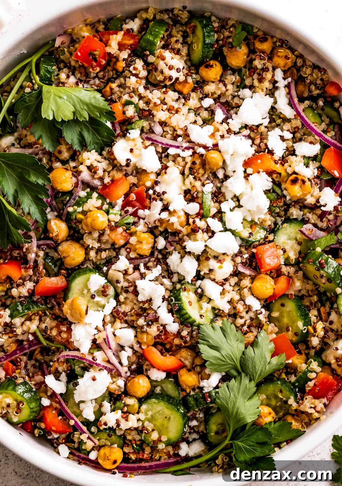 Drizzled with homemade dressing, this Jennifer Aniston quinoa salad with crunchy chickpeas is super light and refreshing. Close up shot of a salad with chickpeas, sliced cucumbers, red onions, peppers, herbs, and feta.
