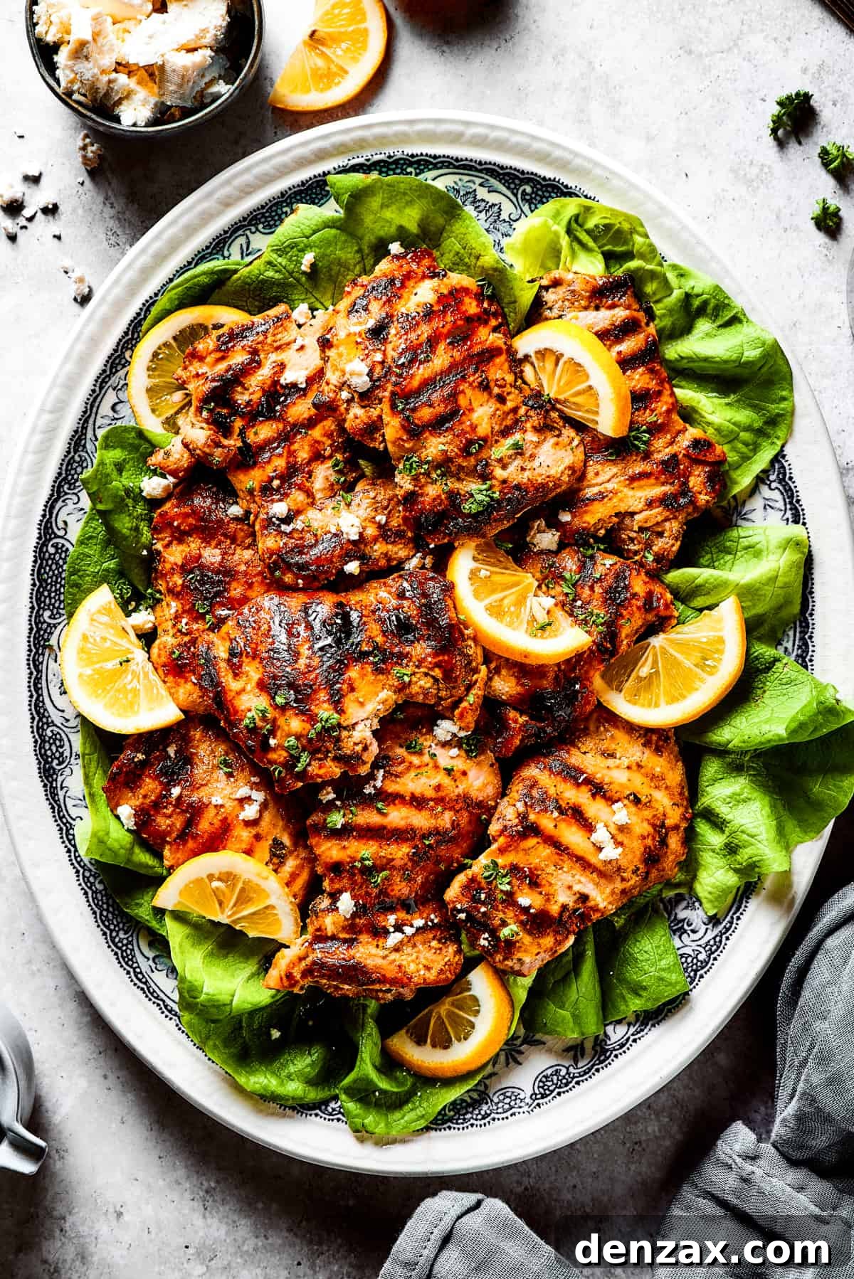 Grilled chicken thighs and lemon slices on a bed of salad greens.
