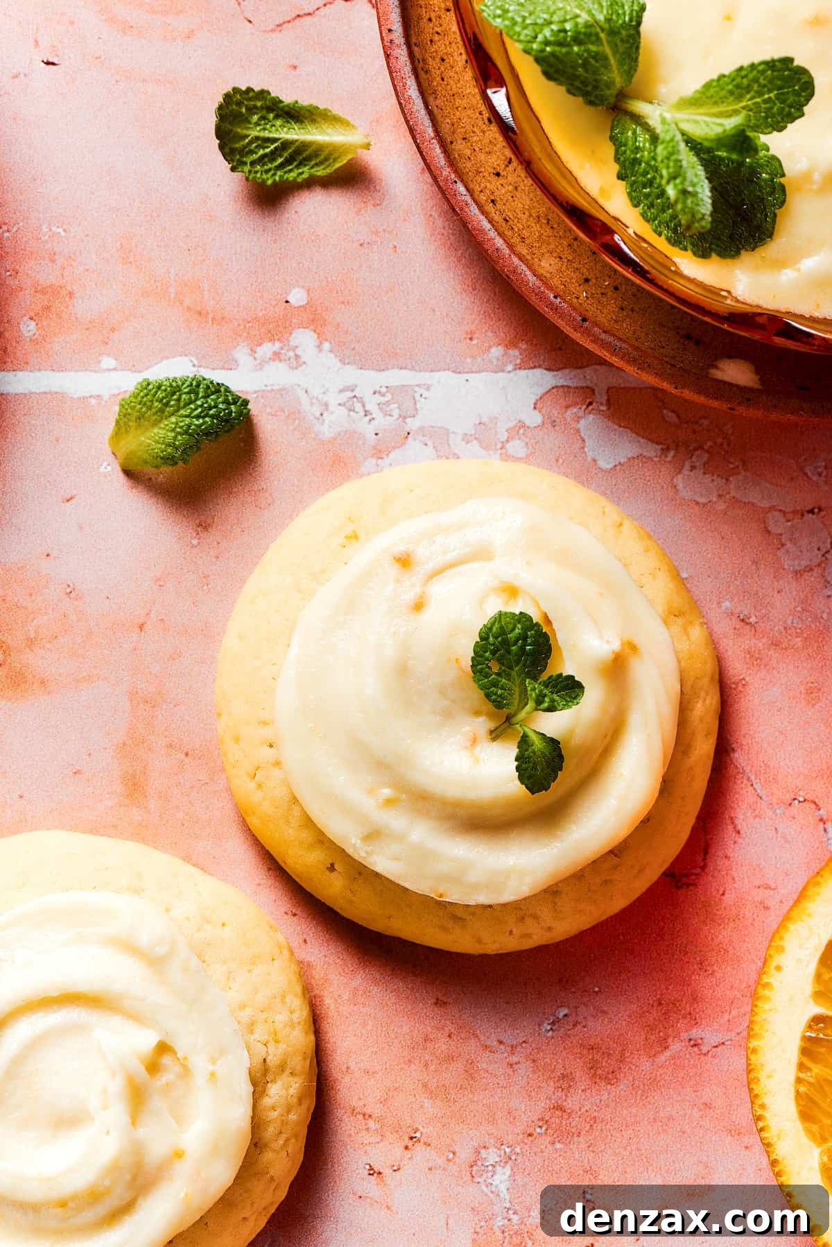 Three orange cookies garnished with fresh herbs, on a tile table.