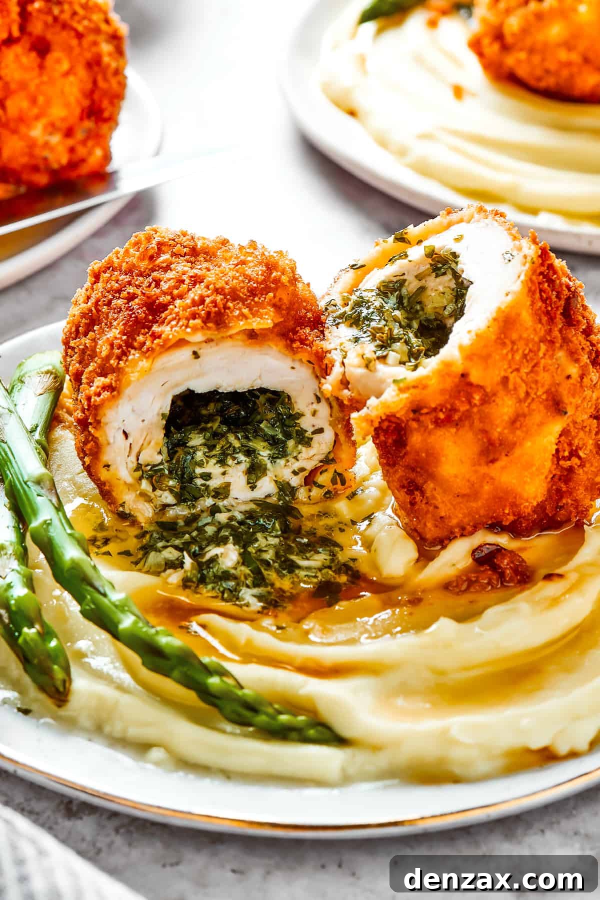 A serving of mashed. potatoes and asparagus with chicken Kiev cut in half to show the buttery filling.
