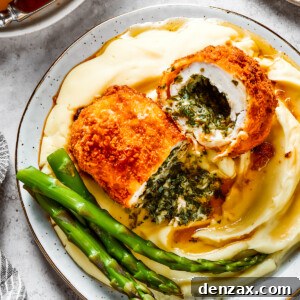 A serving of mashed. potatoes and asparagus with chicken Kiev cut in half to show the buttery filling.