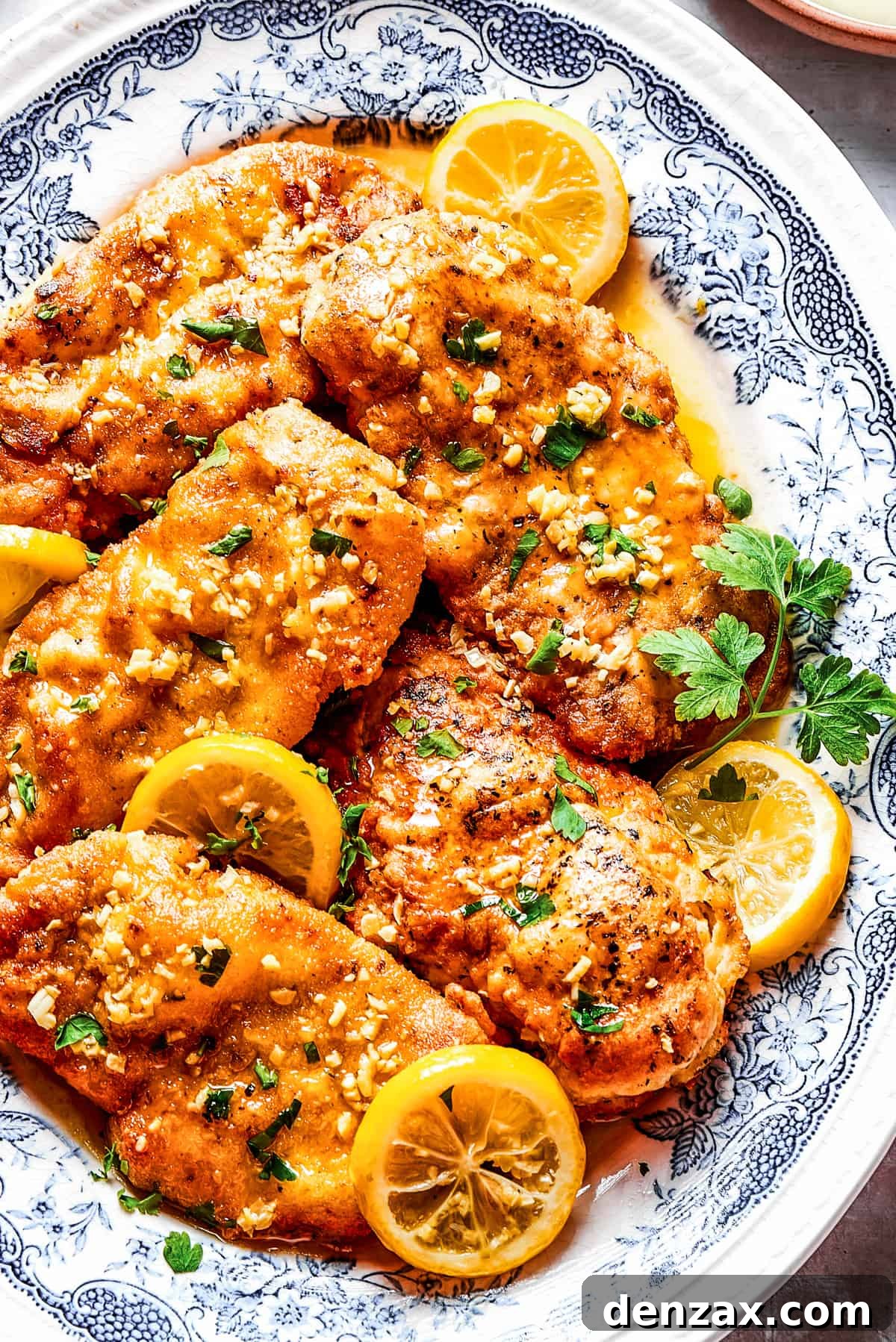 Homemade lemon chicken recipe arranged on a platter with parsley and lemon slices.