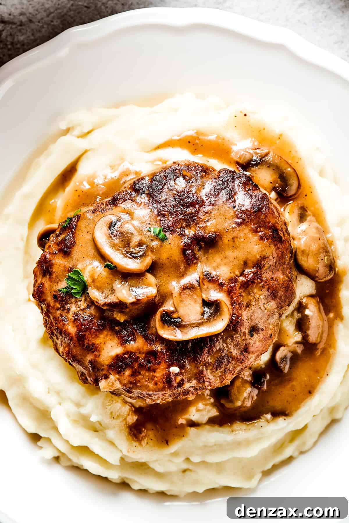 Salisbury steak with mushroom gravy served on a dinner plate over mashed potatoes.