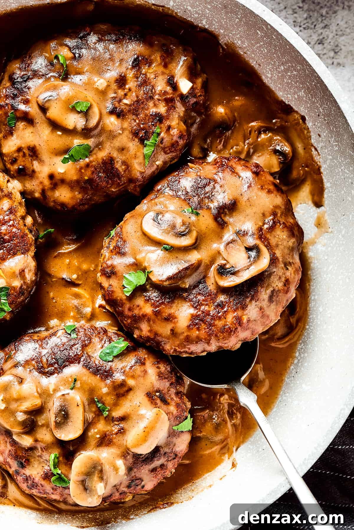 A skillet of homemade beef patties in mushroom and onion gravy.