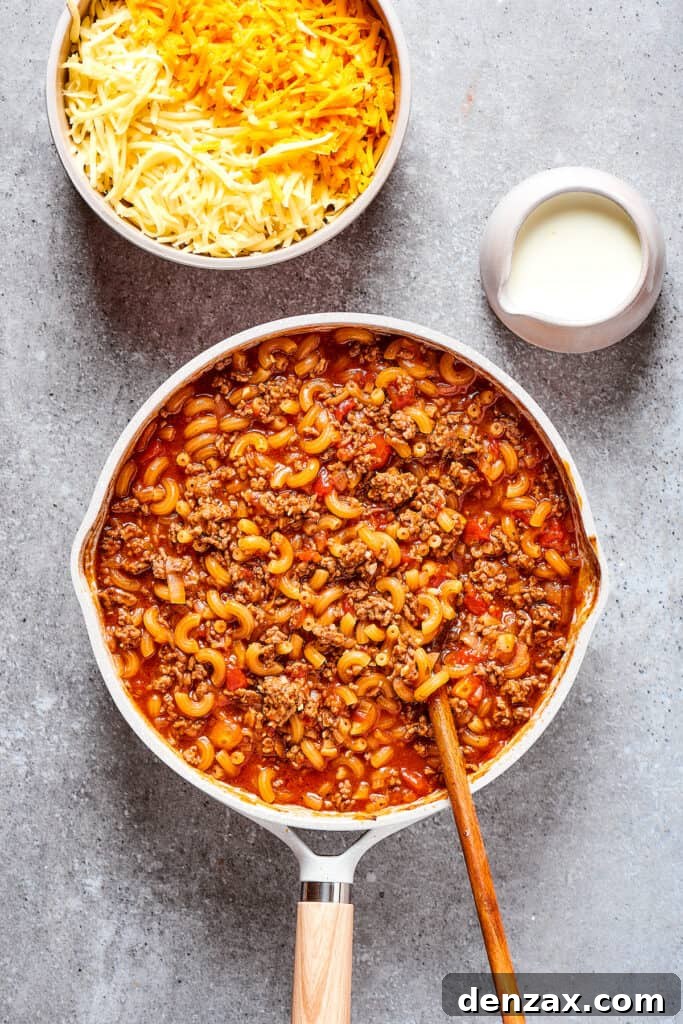 Macaroni pasta cooking in a skillet with sauce and beef.