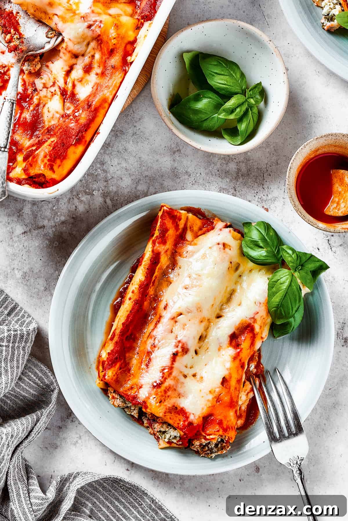 Overhead shot of stuffed manicotti on a plate, next to a casserole dish with a serving spoon resting in it.