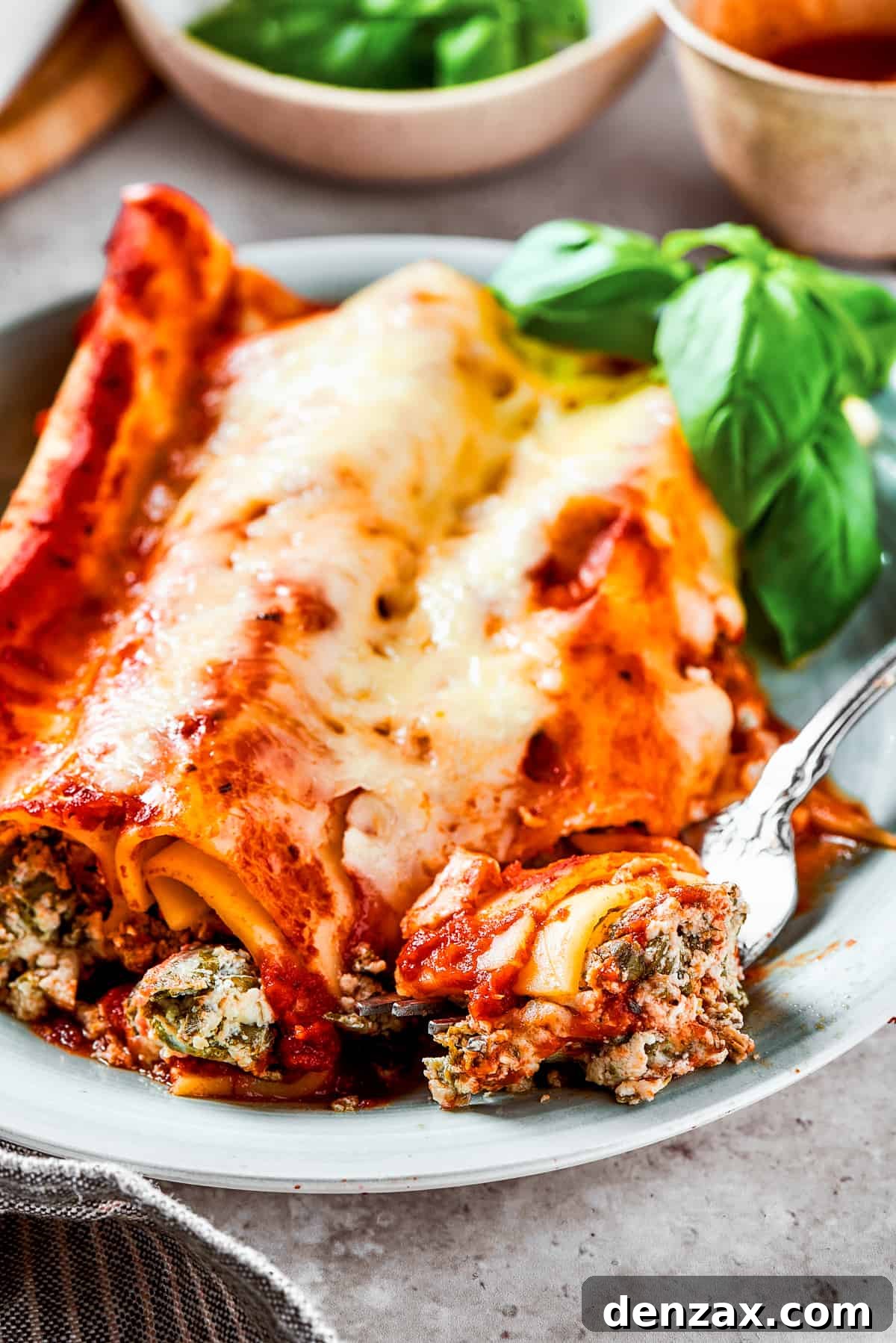 A plate with three stuffed pasta tubes topped with melted cheese and herbs.