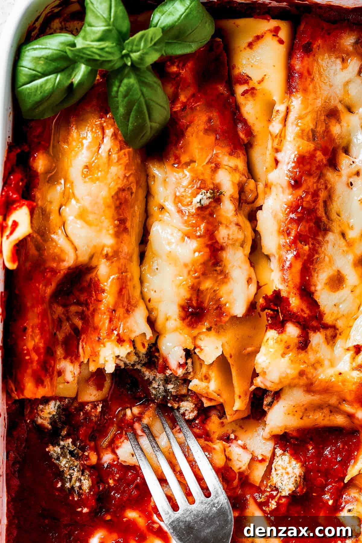 A casserole of baked pasta, with most of it removed from the dish, and a serving fork resting in the dish.