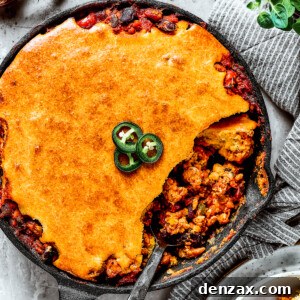 Overhead shot of a cast iron skillet with homemade Chili cornbread casserole and a serving removed with a spoon.