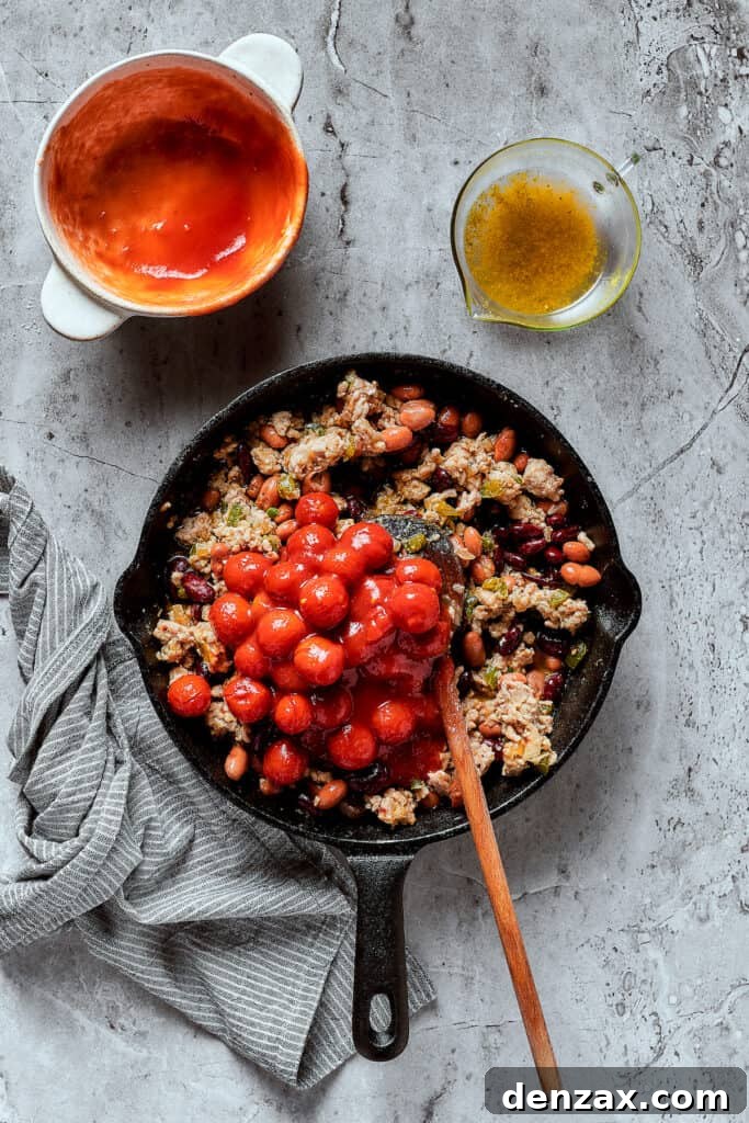 Adding tomatoes and other chili ingredients to a skillet.