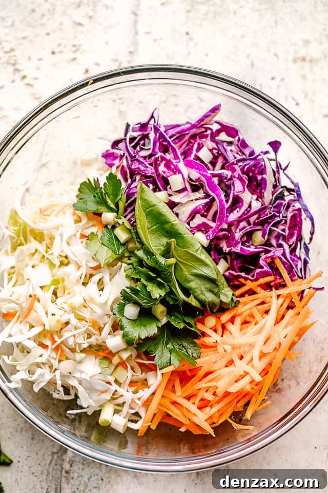 shredded red and green cabbage in a glass bowl with shredded carrots and fresh cilantro.