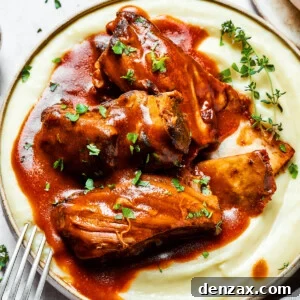 A bowl of mashed potatoes topped with ribs and sauce.