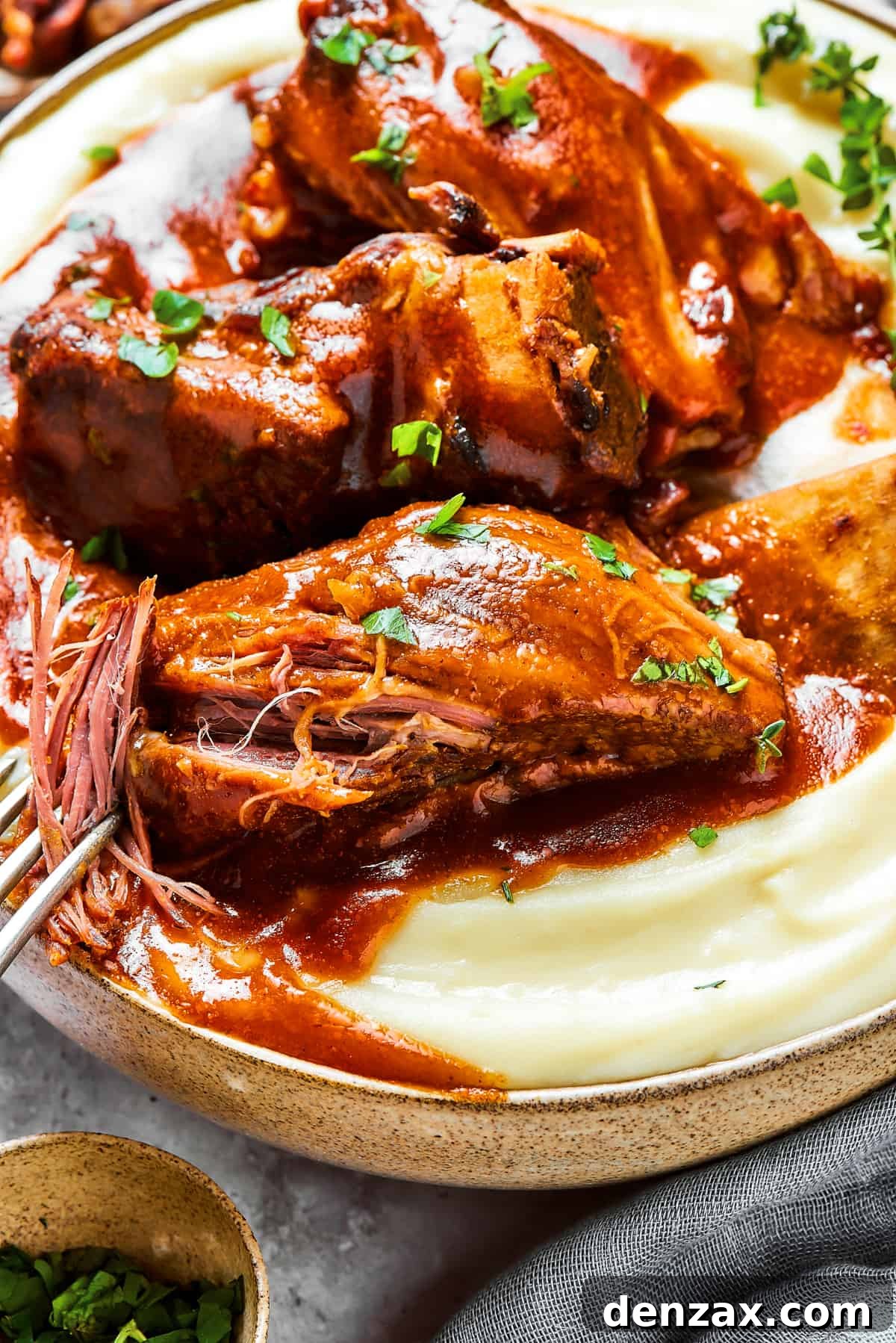 A fork pulling the meat of the short ribs apart, to show its tenderness.