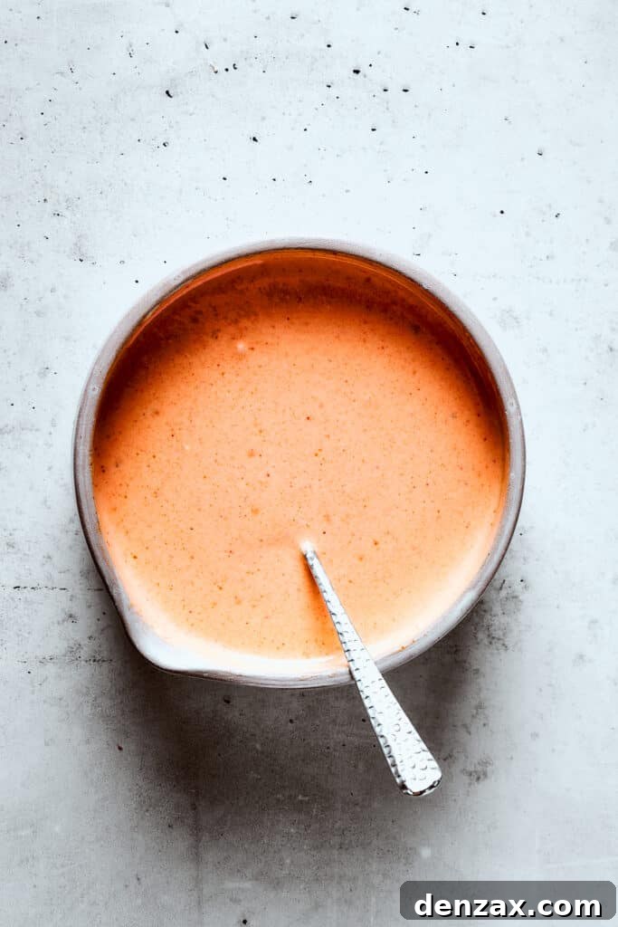 Yum Yum Sauce is a scrumptious, creamy condiment that adds a burst of flavor to any dish. You'll love this sweet, tangy Japanese sauce! Mixing the yum yum sauce with a spoon.