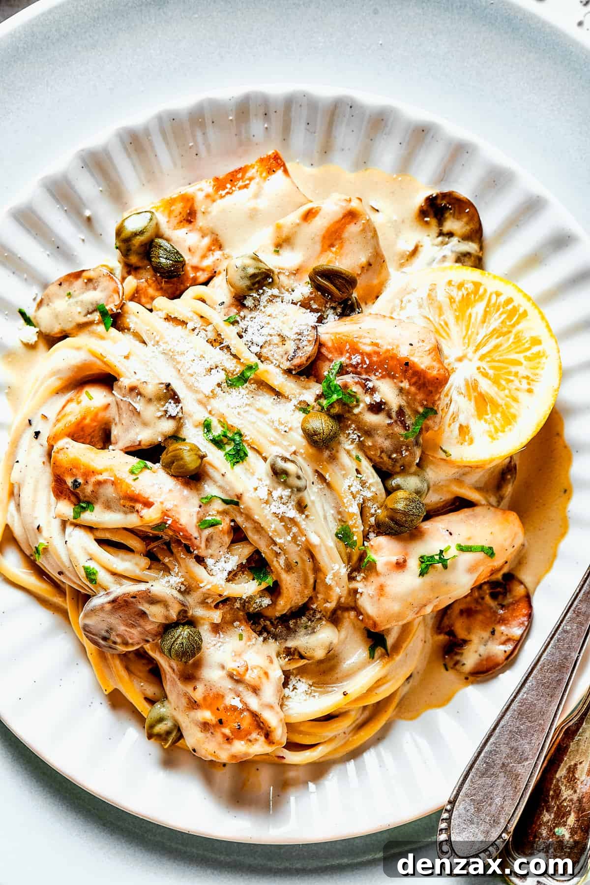 Chicken piccata in caper-lemon sauce with pasta and served on a dinner plate.