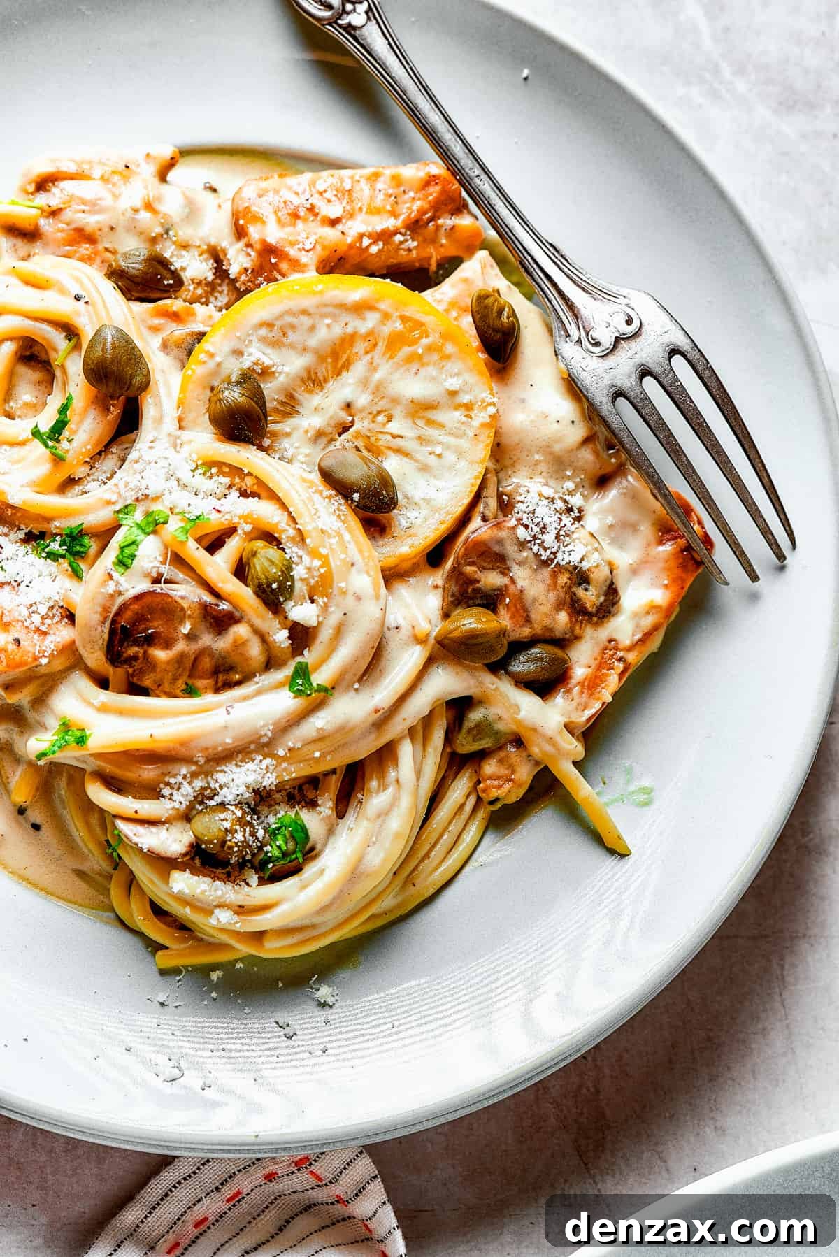Overhead view of a generous helping of chicken pasta on a dinner plate with a fork.