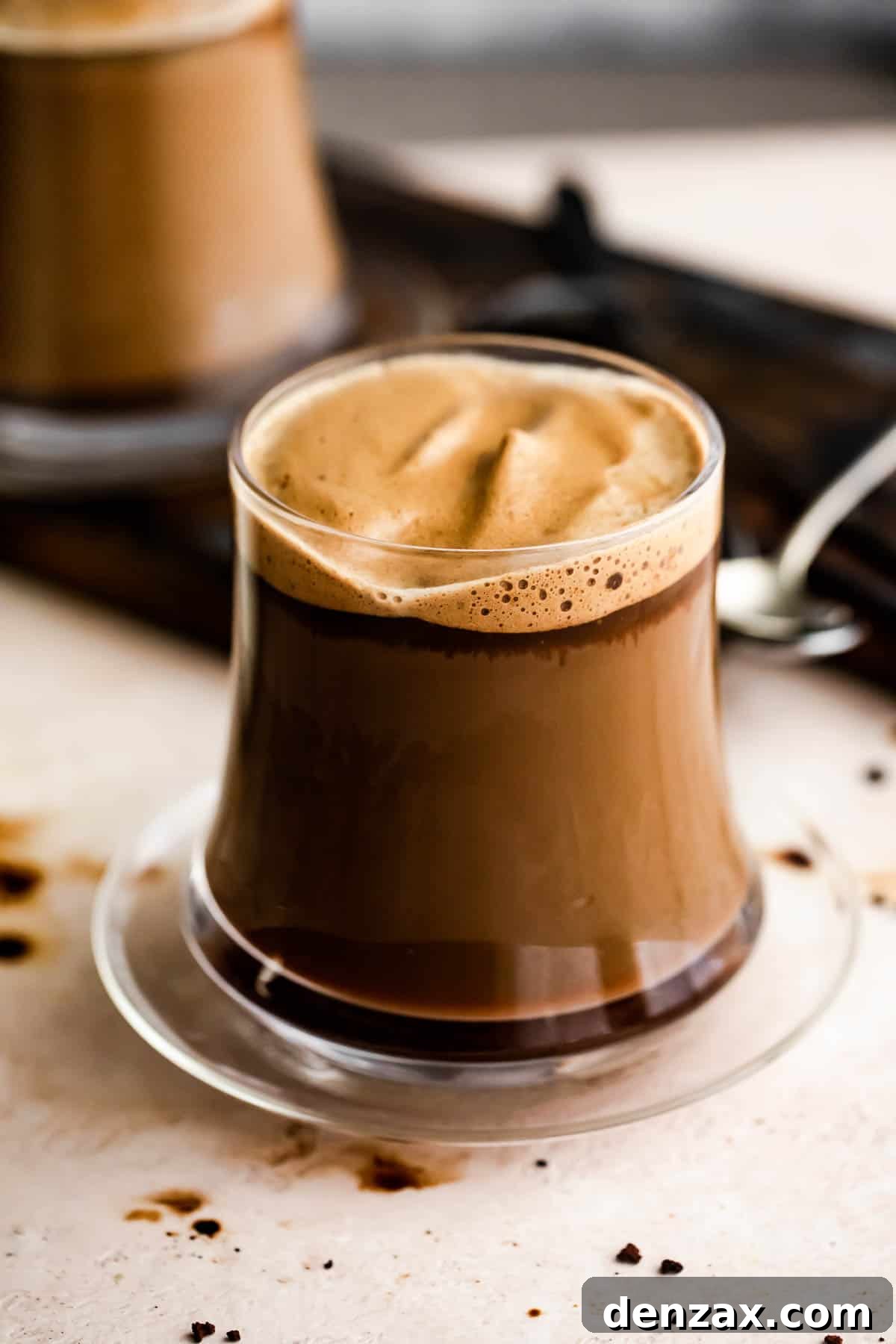 A glass mug with Caffe Macchiato and another mug set right behind it.