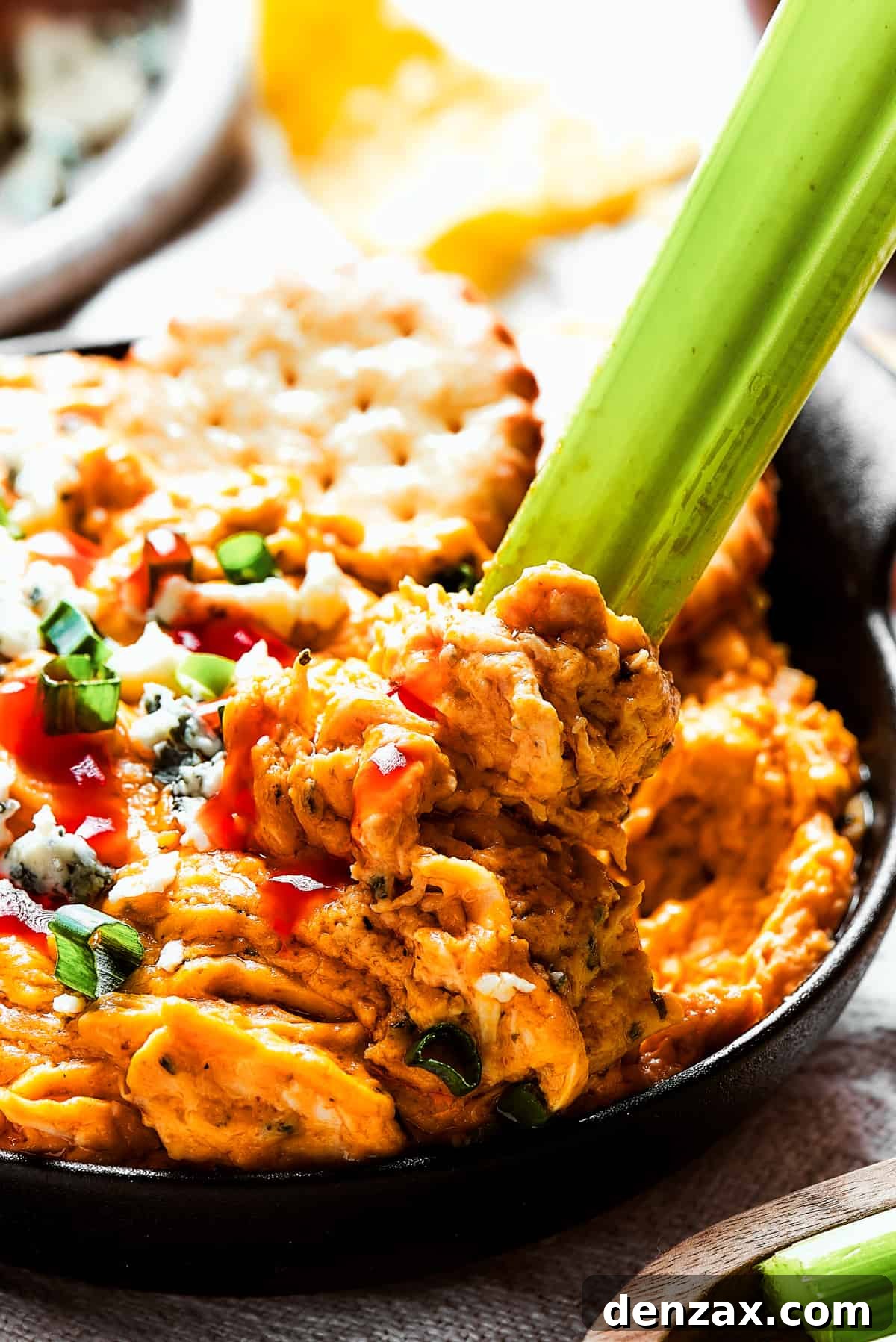 With its creamy, cheesy, spicy goodness, Crockpot Buffalo Chicken Dip is a favorite for parties, game days, movie night, and more! Close-up shot of buffalo chicken dip garnished with blue cheese and green onions and a celery stick dipping in.