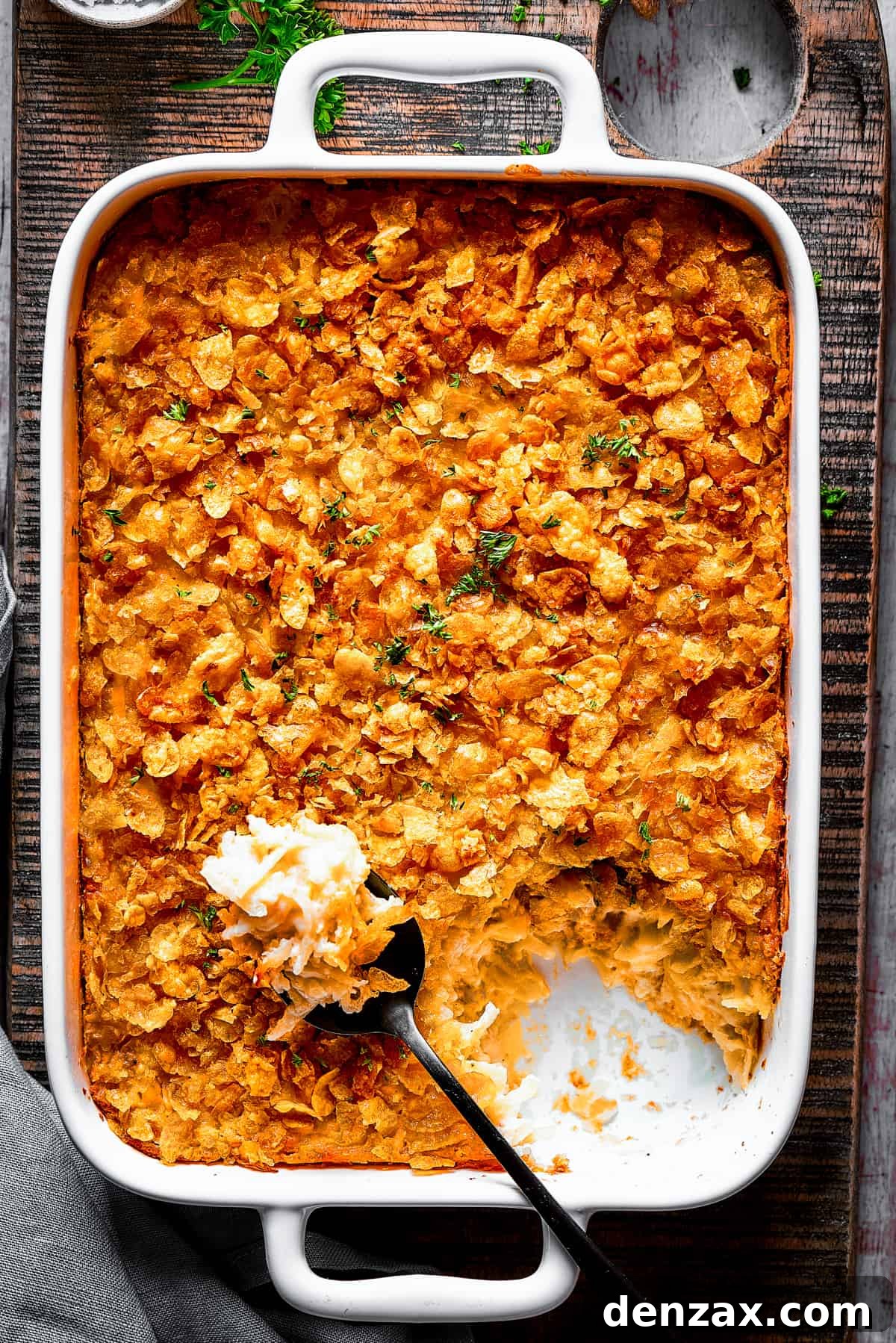 A baking dish with hashbrown casserole. Some of it has been spooned out, and a serving spoon is set on top of the casserole.