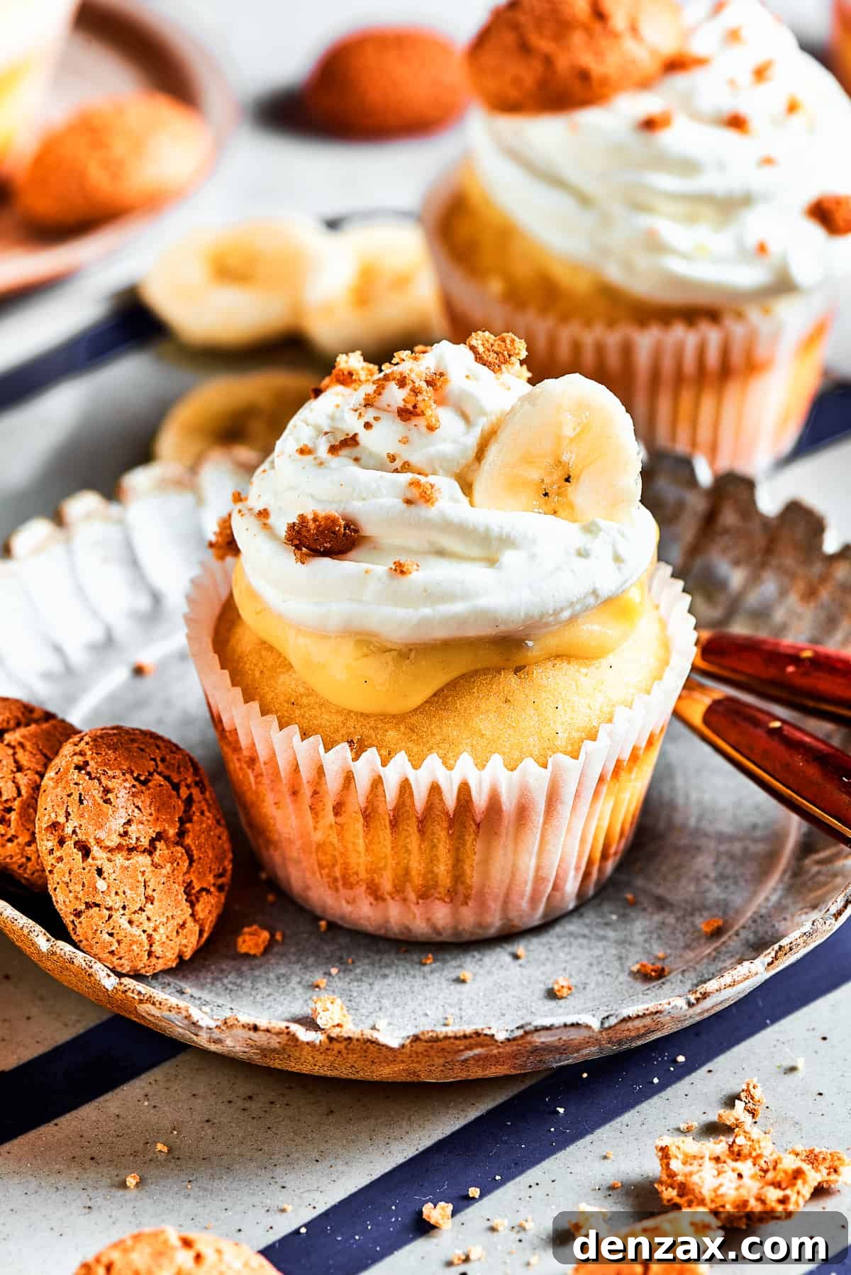 One banana pudding cupcake on a dessert plate. More cupcakes are in the background of the shot.