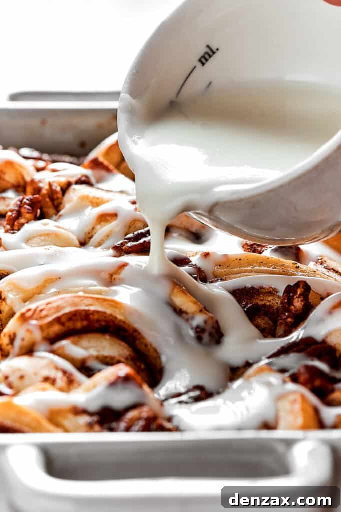 These easy and celebratory cinnamon roll casseroles are rich, creamy, and buttery, and packed with sticky and sweet maple syrup and pecans. Close up of a bowl of icing being poured over cinnamon roll casserole